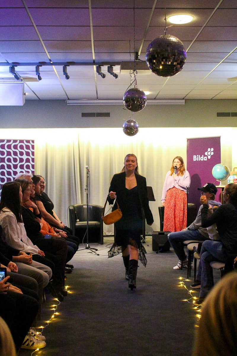Tjej går i en klänning och handväska längs en catwalk med publik