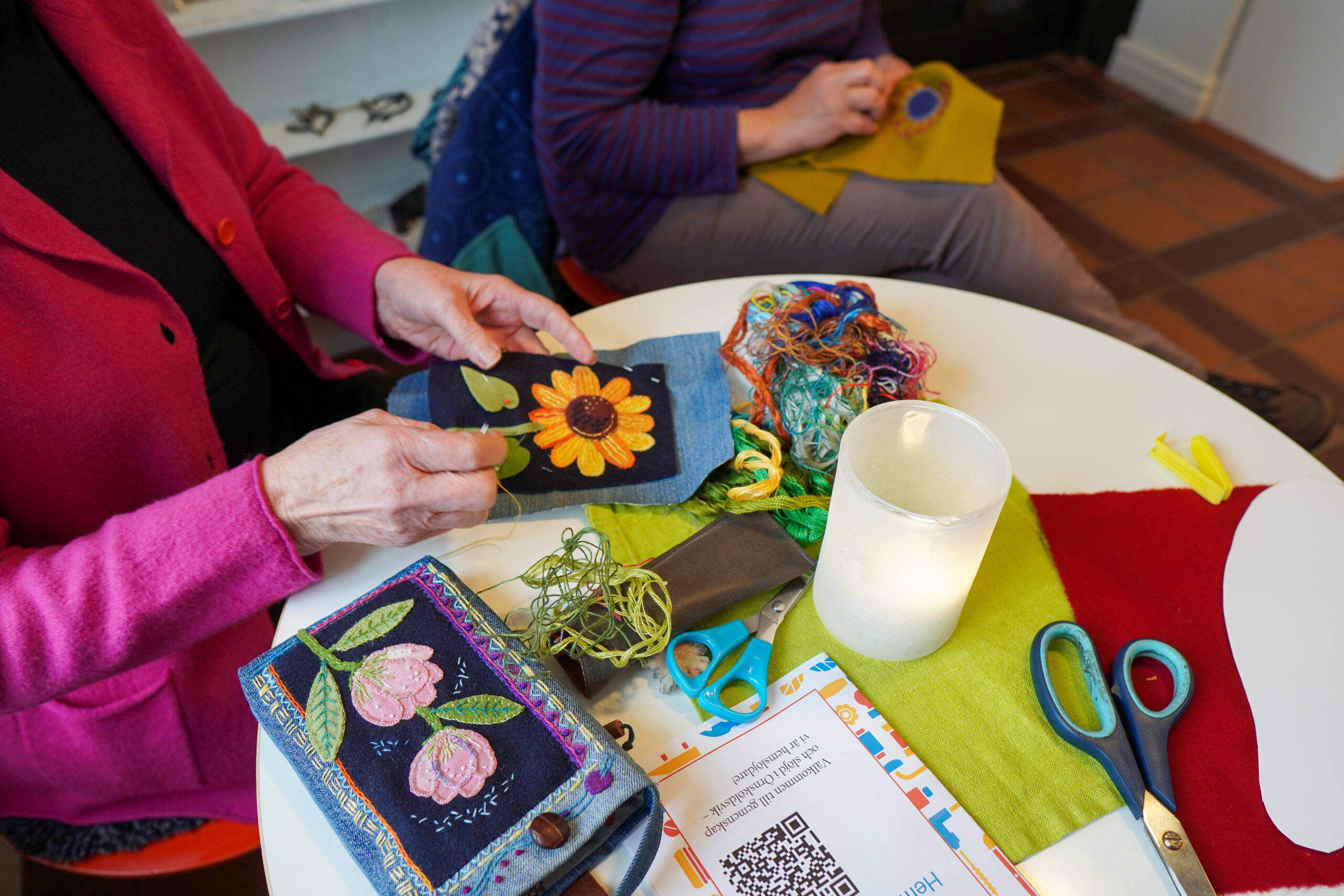 två kvinnor som sitter vid ett bord och broderar