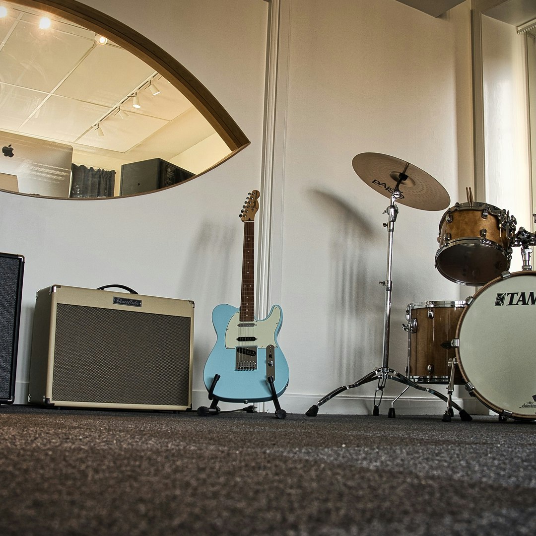 Ett rum med trumset, gitarr, förstärkare och spegel.