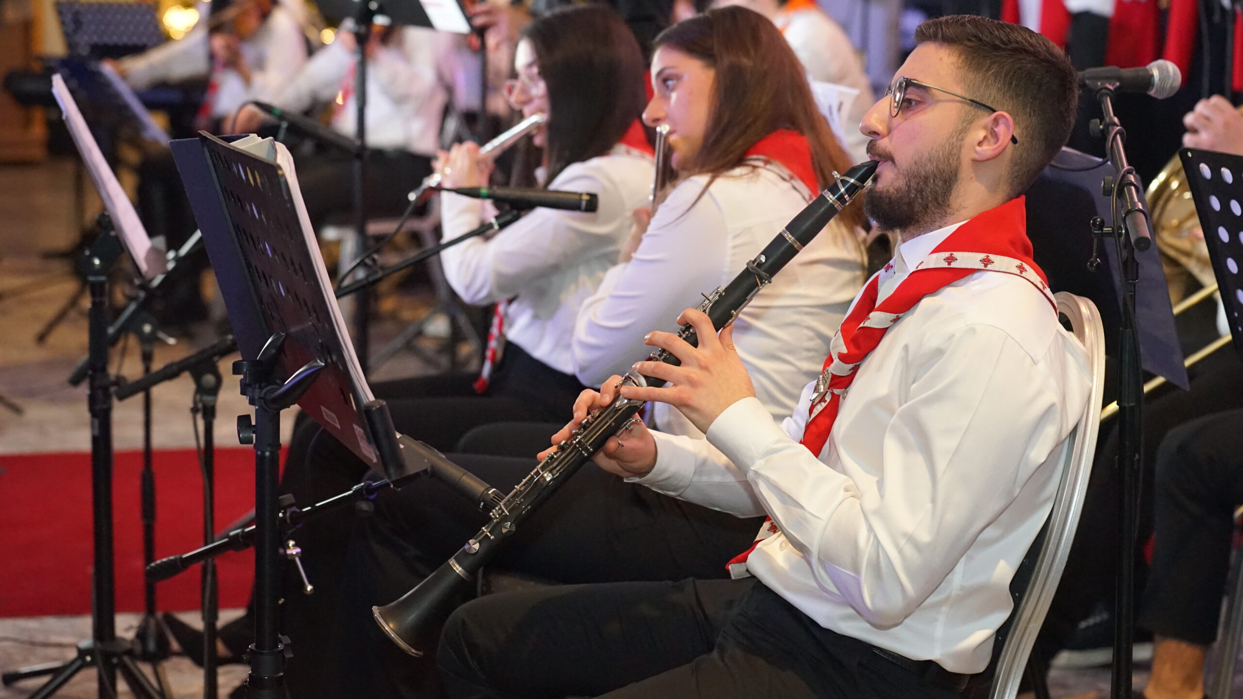 Musiker i vita skjortor och röda halsdukar spelar klarinetter i en orkester.