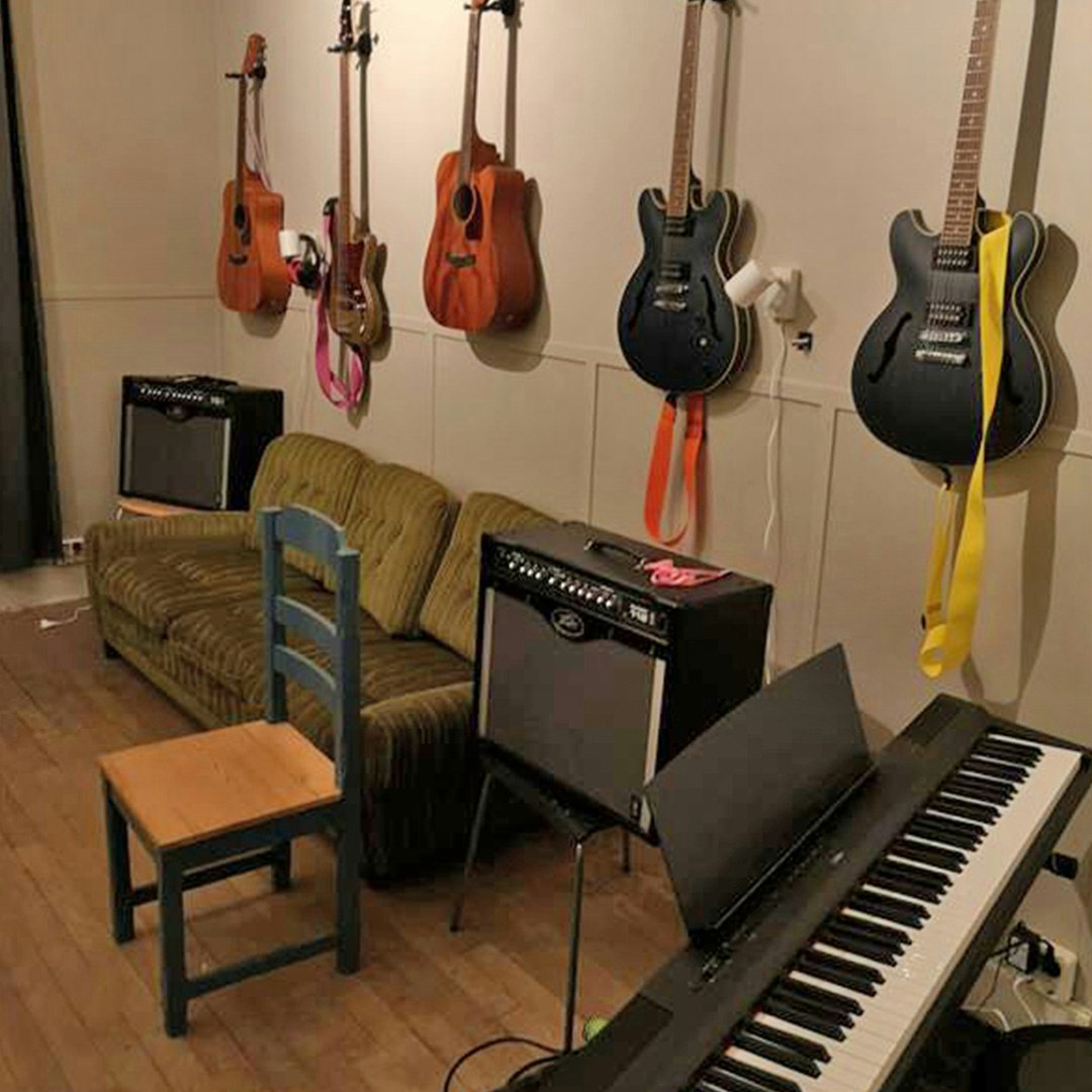 Ett musikrum med fem gitarrer hängande på väggen, två förstärkare, ett keyboard, en grön soffa och en trästol.