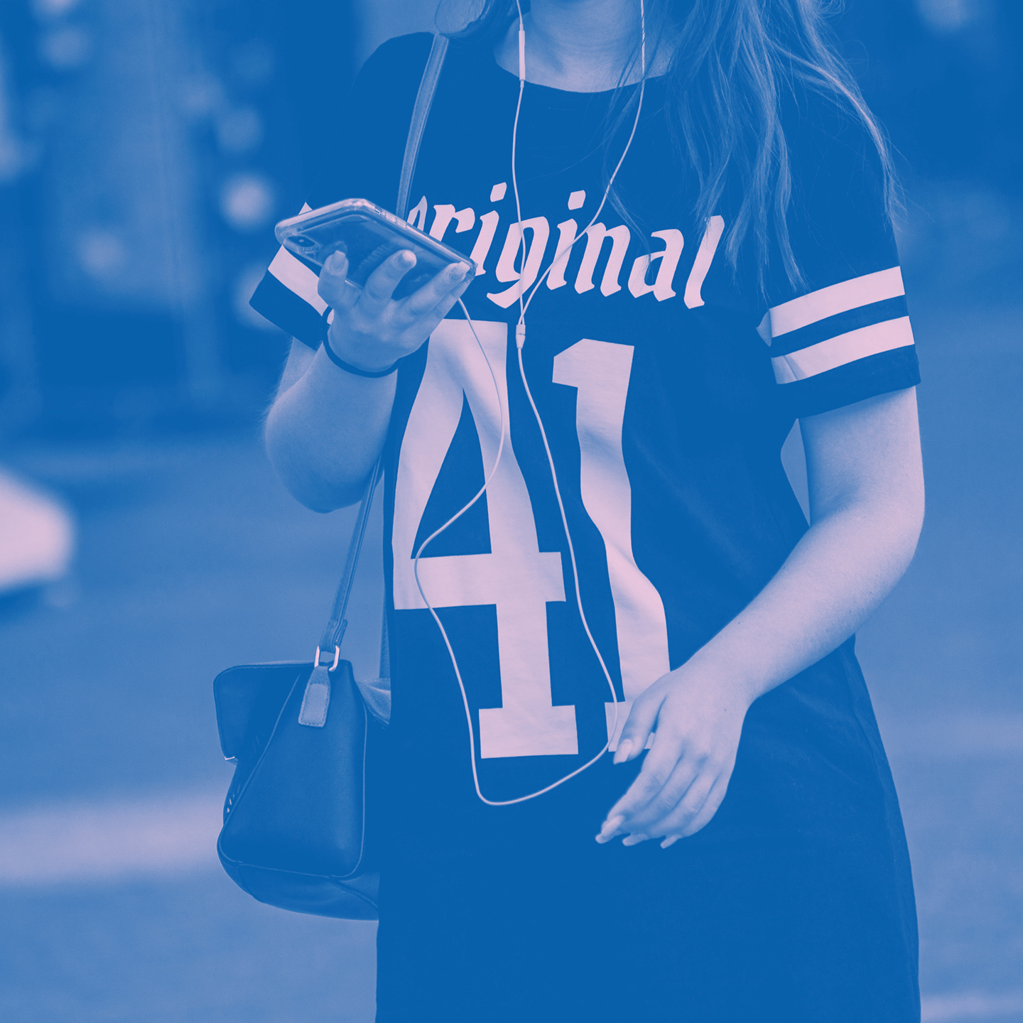 Person iförd en "Original 41"-tröja, håller i en telefon med hörlurar och en crossbody-väska.