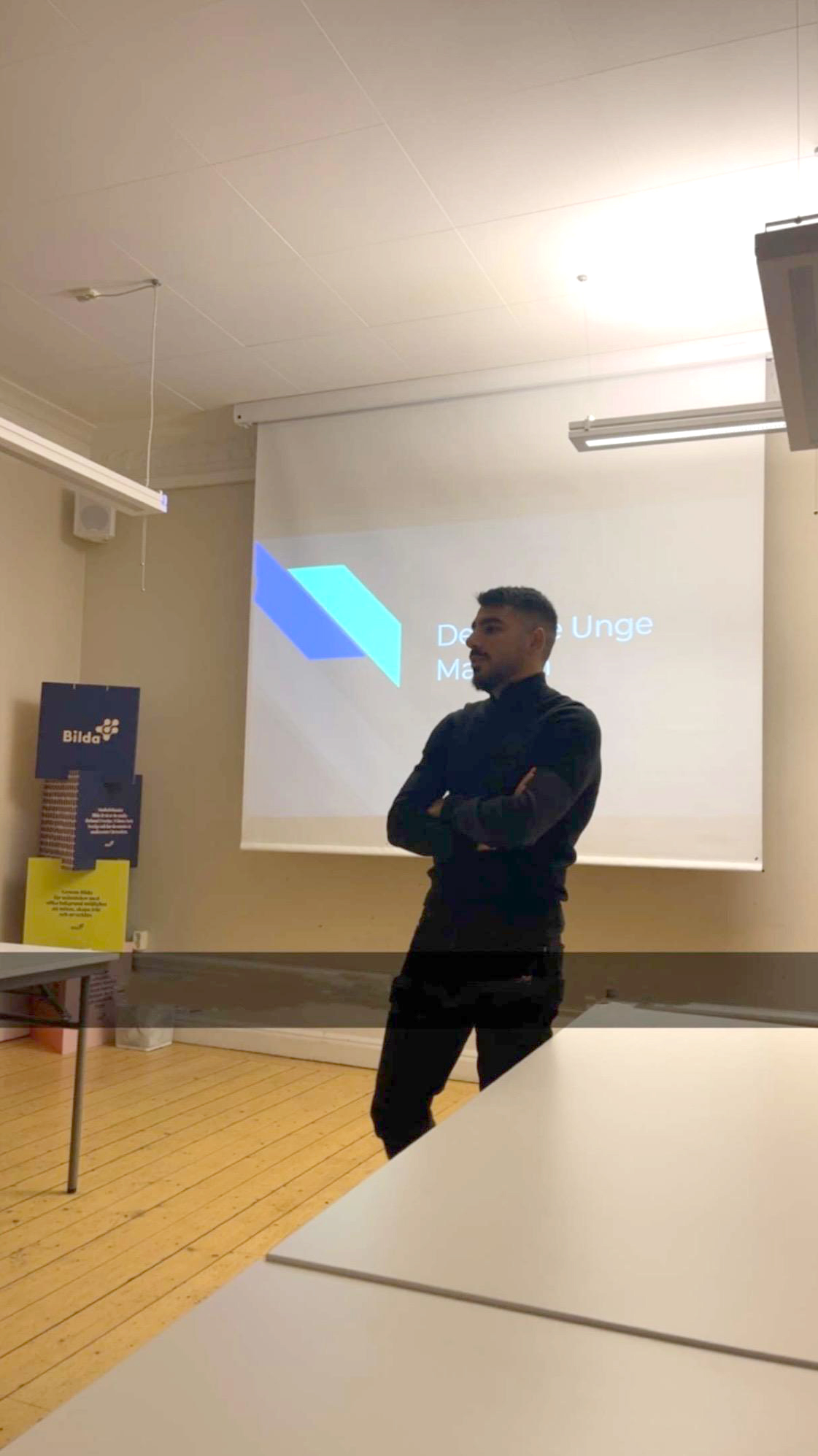 Svartklädd man står framför en projicerad presentation i ett klassrum eller mötesrum.