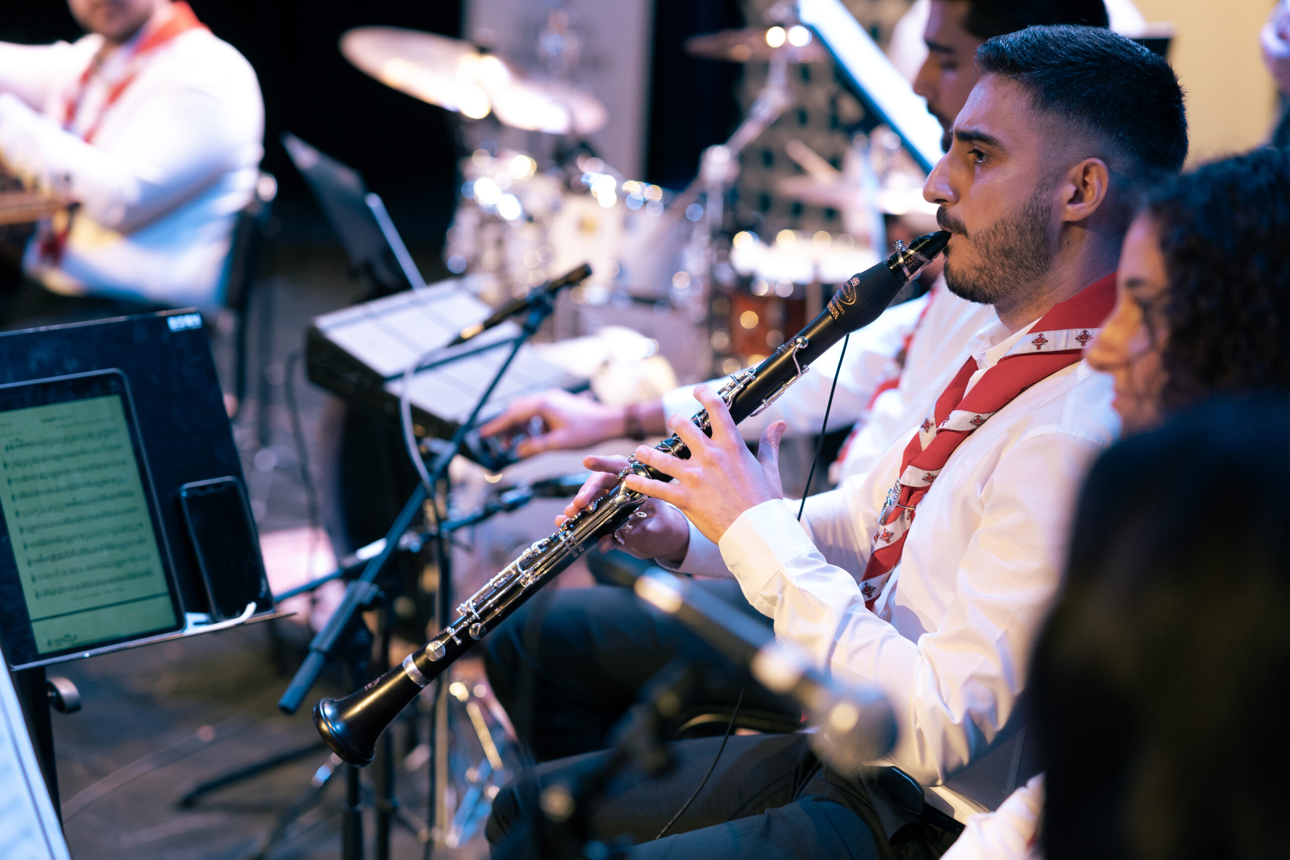 En man i vit skjorta spelar klarinett i en orkester under ett liveframträdande.