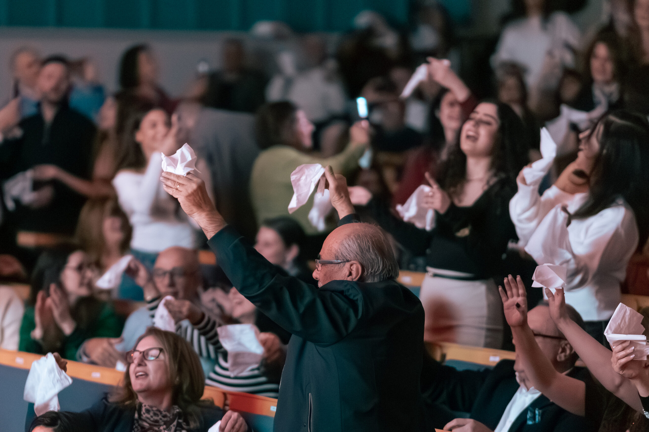 Personer i en publik som viftar med vita näsdukar och jublar under ett livligt evenemang eller framträdande.