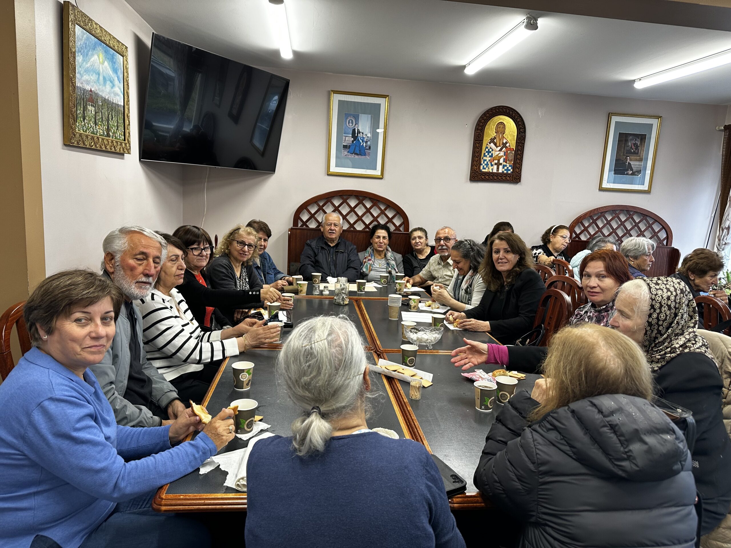 En grupp äldre vuxna sitter runt borden, ler och njuter av drinkar i ett mysigt, inrett rum.