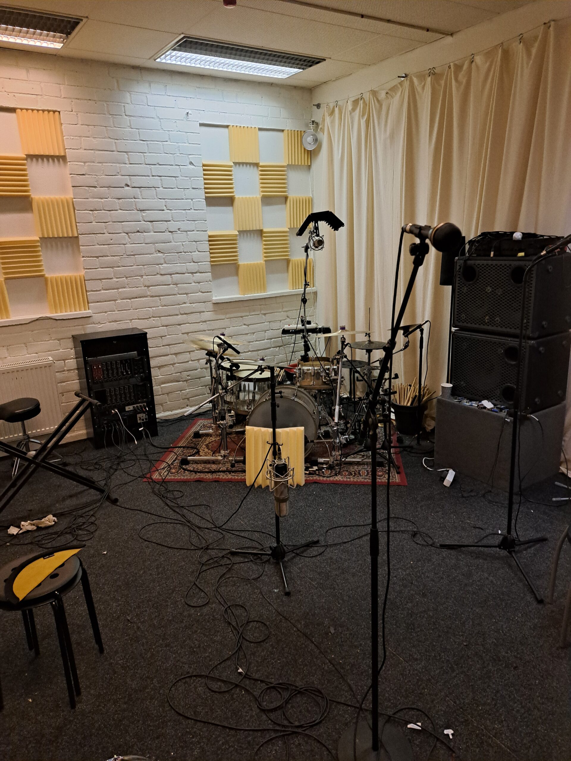 En musikstudio med trumset, mikrofoner, högtalare och ljudisolerande skumplastpaneler på väggarna.